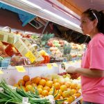 A grocer stands in front of her fresh produce cooler.