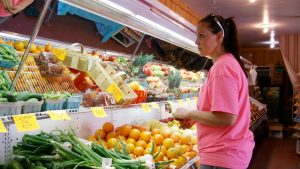 A grocer stands in front of her fresh produce cooler.